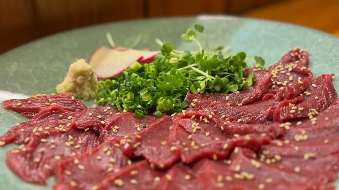 ねぎや薬味、ごまを添えた赤身肉の一皿